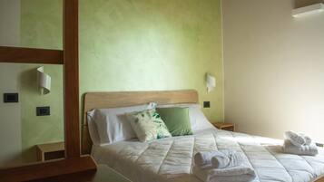 Un letto ben rifatto con biancheria bianca e cuscini verdi, una testiera in legno e un comodino con una lampada.