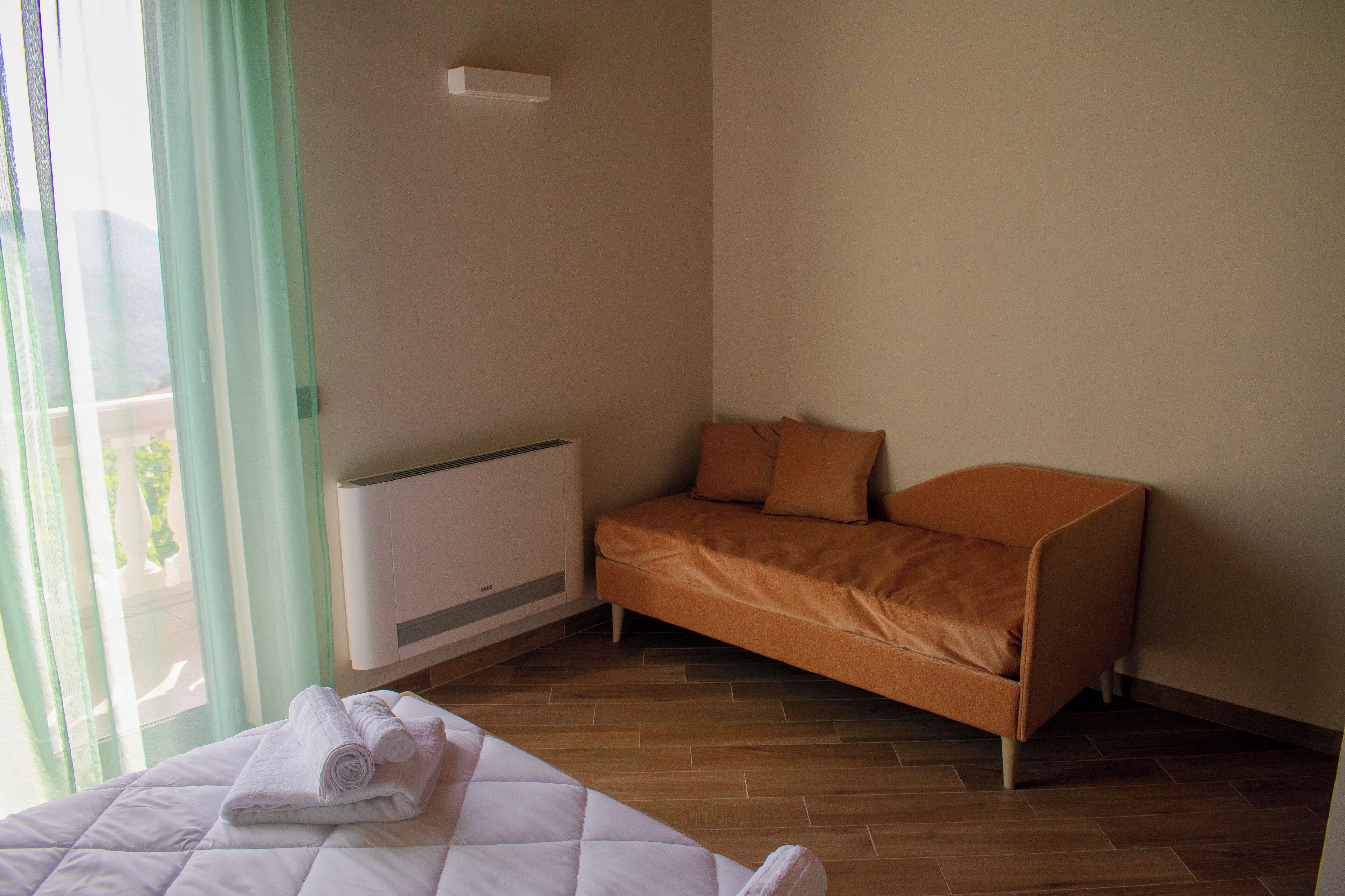 Habitació d'hotel amb un llit, un sofà, una finestra amb cortines i un aire condicionat fixat a la paret.