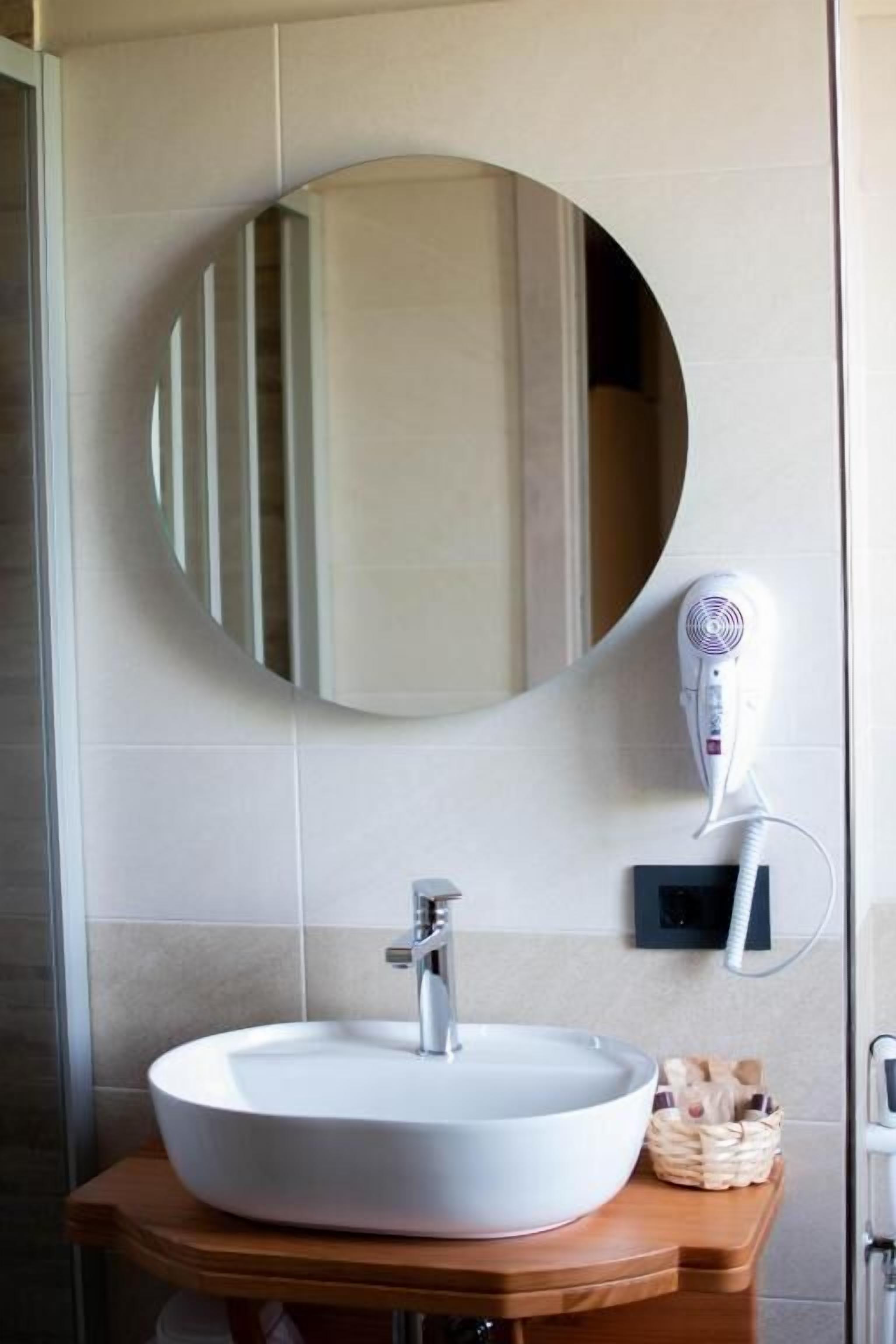 Une salle de bain avec un miroir rond, un lavabo blanc et un sèche-cheveux fixé au mur.