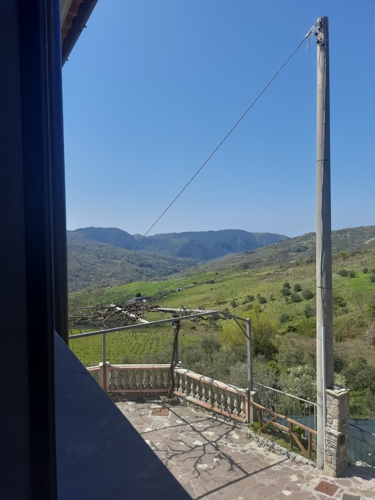 Un balcón con suelo de piedra y barandilla de metal, con vistas a un paisaje montañoso.