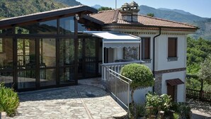 A modern house with a glass extension, stone patio, and a view of the mountains. - B&B La Casetta (Verbicaro)