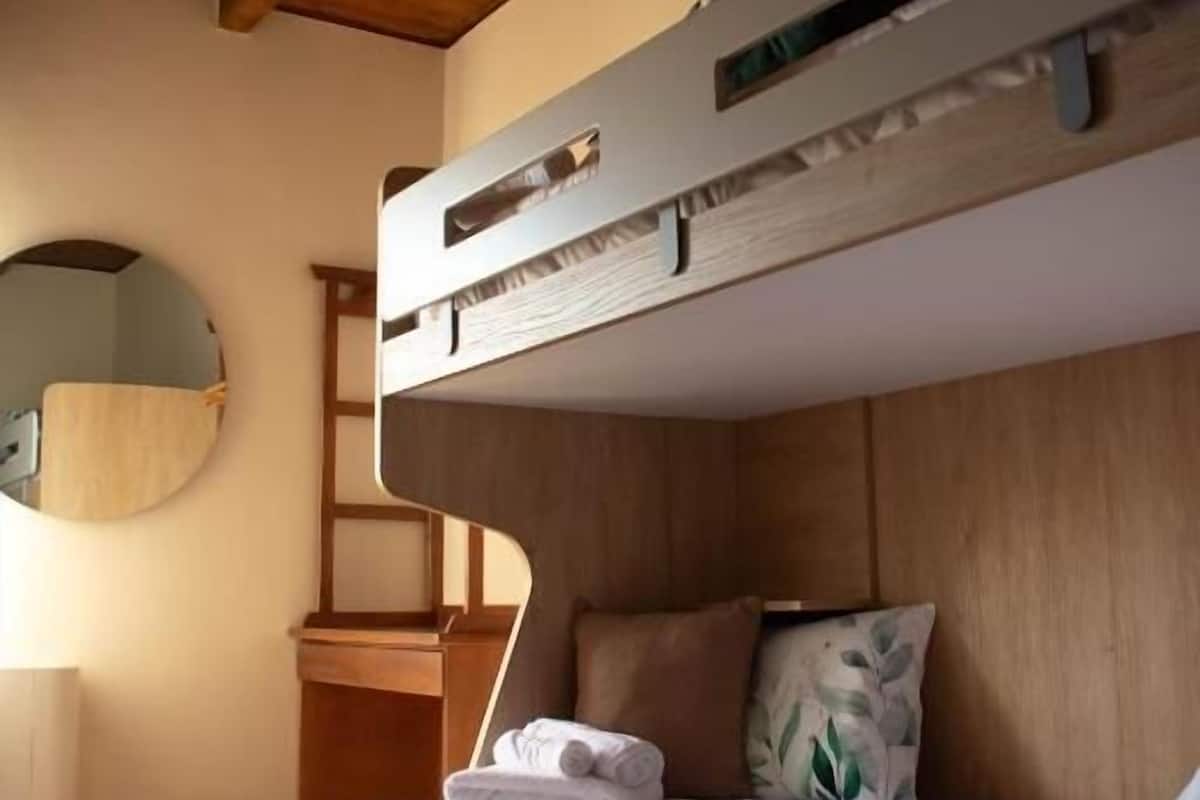 Une chambre à coucher avec un lit superposé, une tête de lit en bois, une table de chevet, un miroir et une fenêtre.