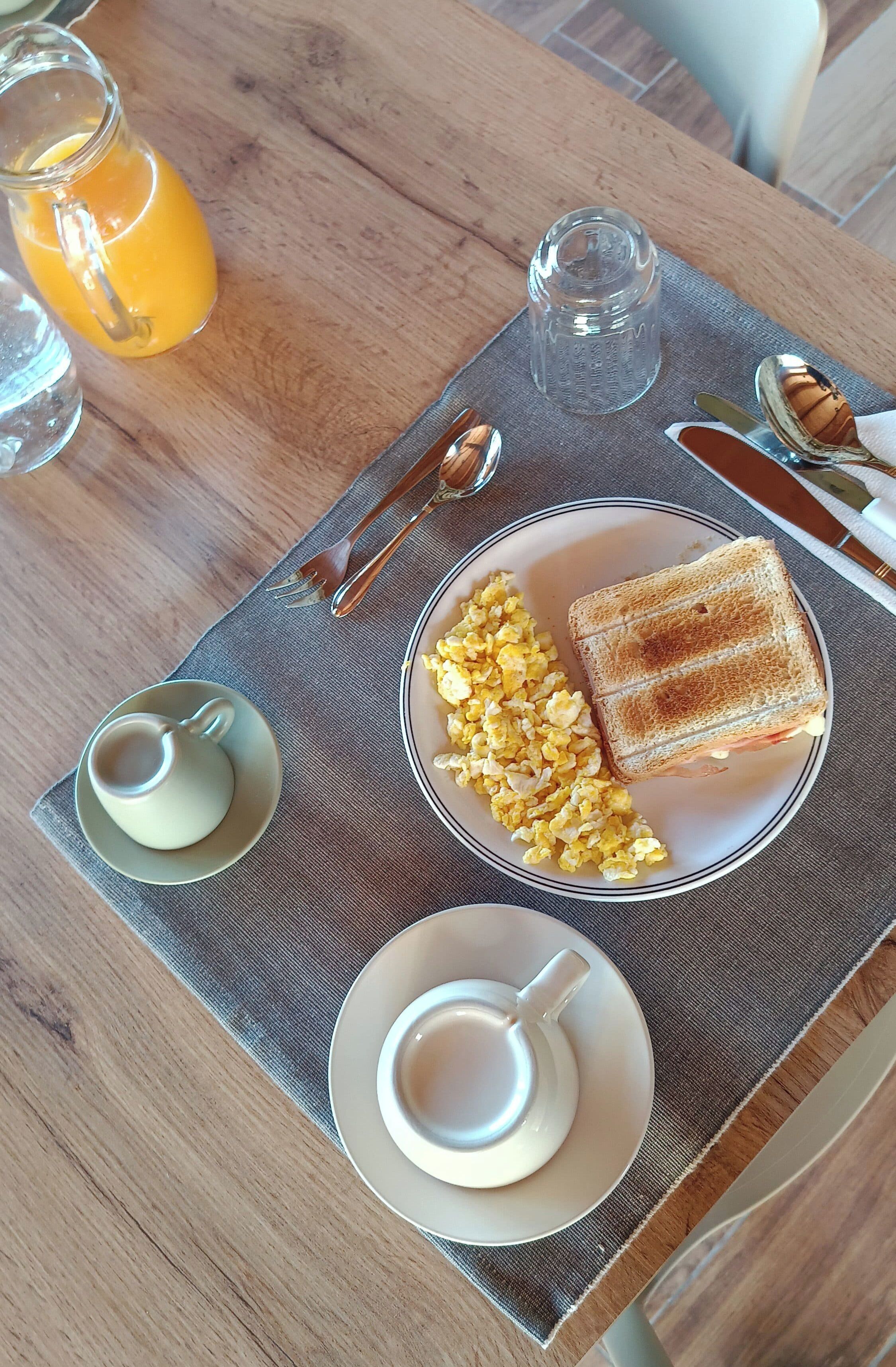 Bandeja de desayuno con tostadas, huevos revueltos y un vaso de jugo de naranja sobre una mesa de madera.