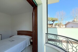 Un dormitorio con una cama, una mesita de noche y ventana con vista a una zona residencial.