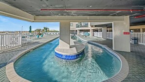 A swimming pool with a hot tub, surrounded by a deck area with lounge chairs and a view of a building in the background. - Ocean Bay Club 1510-4 Bedroom-Indoor/Outdoor Pools (North Myrtle Beach)