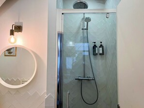 Een douche met glazen wanden, voorzien van een handdouche en een spuitmondje, bevestigd aan een betegelde muur.