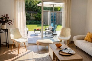 A modern living room with a sofa, two chairs, a coffee table, and a view of a garden through a glass door. - Cosy house 4 bedrooms, Saint-Coulomb center, beaches 5mn (Saint-Coulomb)