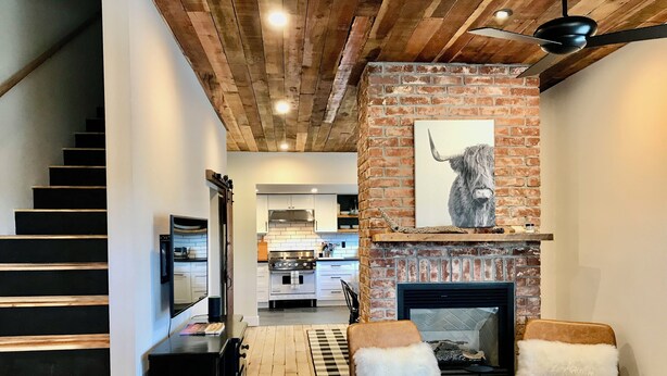 A modern interior with a staircase, a fireplace, and a kitchen in the background. - Walk to NAU & Downtown - 2BR Historic Home w/ AC, Fireplace, Chef’s Kitchen (Flagstaff)