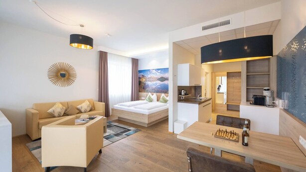 A modern hotel room with a sofa, a dining table with chairs, a kitchen area, and a large window with curtains. - Suite With Character I Graz-süd for 2 24-7 Check-in (Graz)