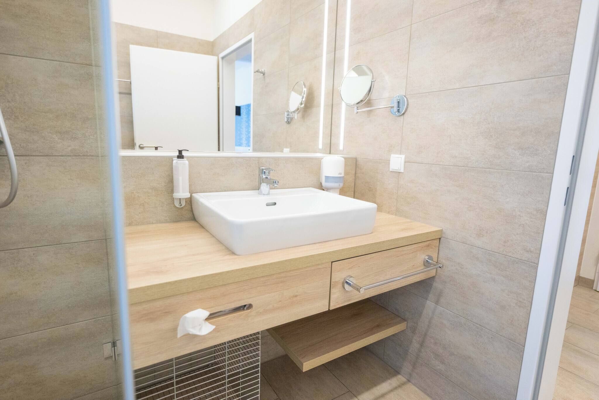 A modern bathroom with a white sink, wooden vanity, two mirrors, and a towel rack.