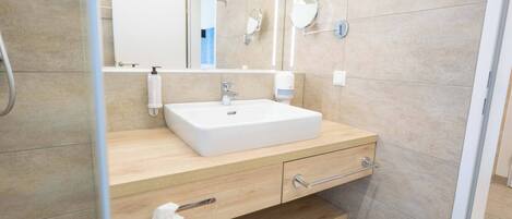 A modern bathroom with a white sink, wooden vanity, two mirrors, and a towel rack.