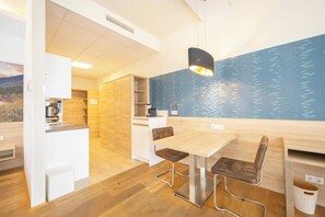 A modern kitchen with wooden cabinets, a dining table with chairs, and a blue wall with a water pattern. - Suite With Character I Graz-süd for 2 24-7 Check-in (Graz)