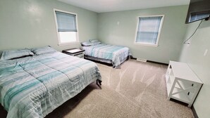 A bedroom with two beds, a small table, and a white cabinet. - Lake Erie Fisherman’s Retreat – 3BR Home in Vermilion with boat parking space. (Vermilion)