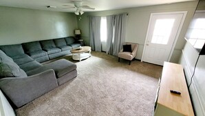 A living room with a sofa, a small table, a chair, and a door. - Lake Erie Fisherman’s Retreat – 3BR Home in Vermilion with boat parking space. (Vermilion)