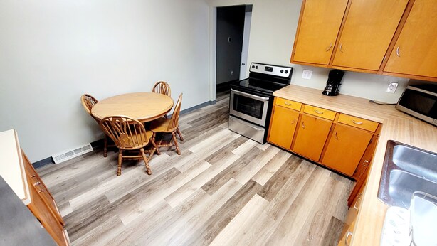 A compact kitchen with a dining table, chairs, a stove, oven, and wooden cabinets. - Lake Erie Fisherman’s Retreat – 3BR Home in Vermilion with boat parking space. (Vermilion)