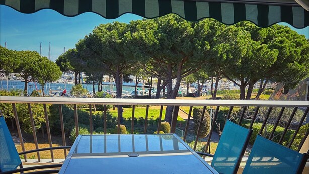 A covered outdoor seating area with a table and chairs, overlooking a marina with boats and trees. - Studio by the sea with pool (Le Grau-du-Roi)