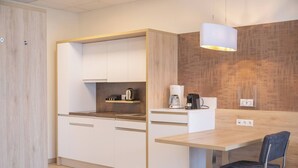 Una cocina moderna con armarios blancos, encimera de madera, cafetera y una silla.