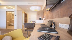 Una habitación de hotel moderna con un escritorio de madera, una computadora portátil, un cuaderno y una silla amarilla.