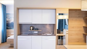 Una kitchenette compacta con gabinetes blancos, una encimera y un lavamanos.