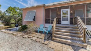A pink building with a covered porch, a wooden staircase, and two blue chairs. - The Rookery 3501 (Gulf Shores)