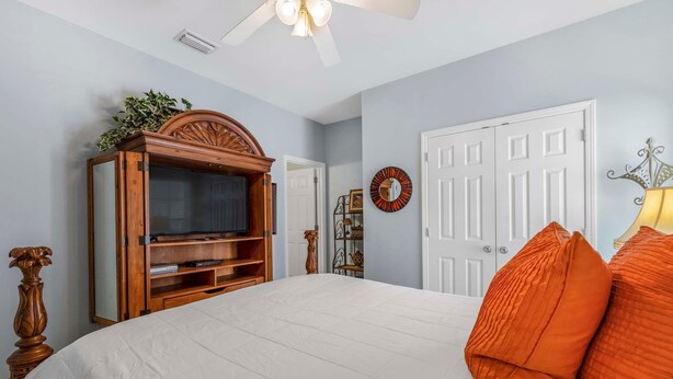 A bedroom with a bed, a wooden entertainment unit, a white door, and a ceiling fan. - The Rookery 3501 (Gulf Shores)