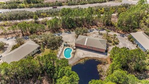A large building with a swimming pool, surrounded by dense trees and a small body of water. - The Rookery 3501 (Gulf Shores)