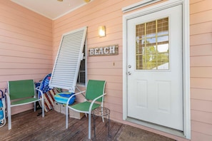 A porch with two green chairs, a bench, a small table, a basket, and a door with a 'BEACH' sign.