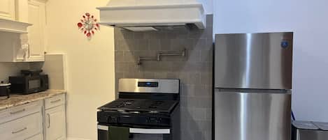 A kitchen with a stainless steel refrigerator, a black stove, and white cabinets.