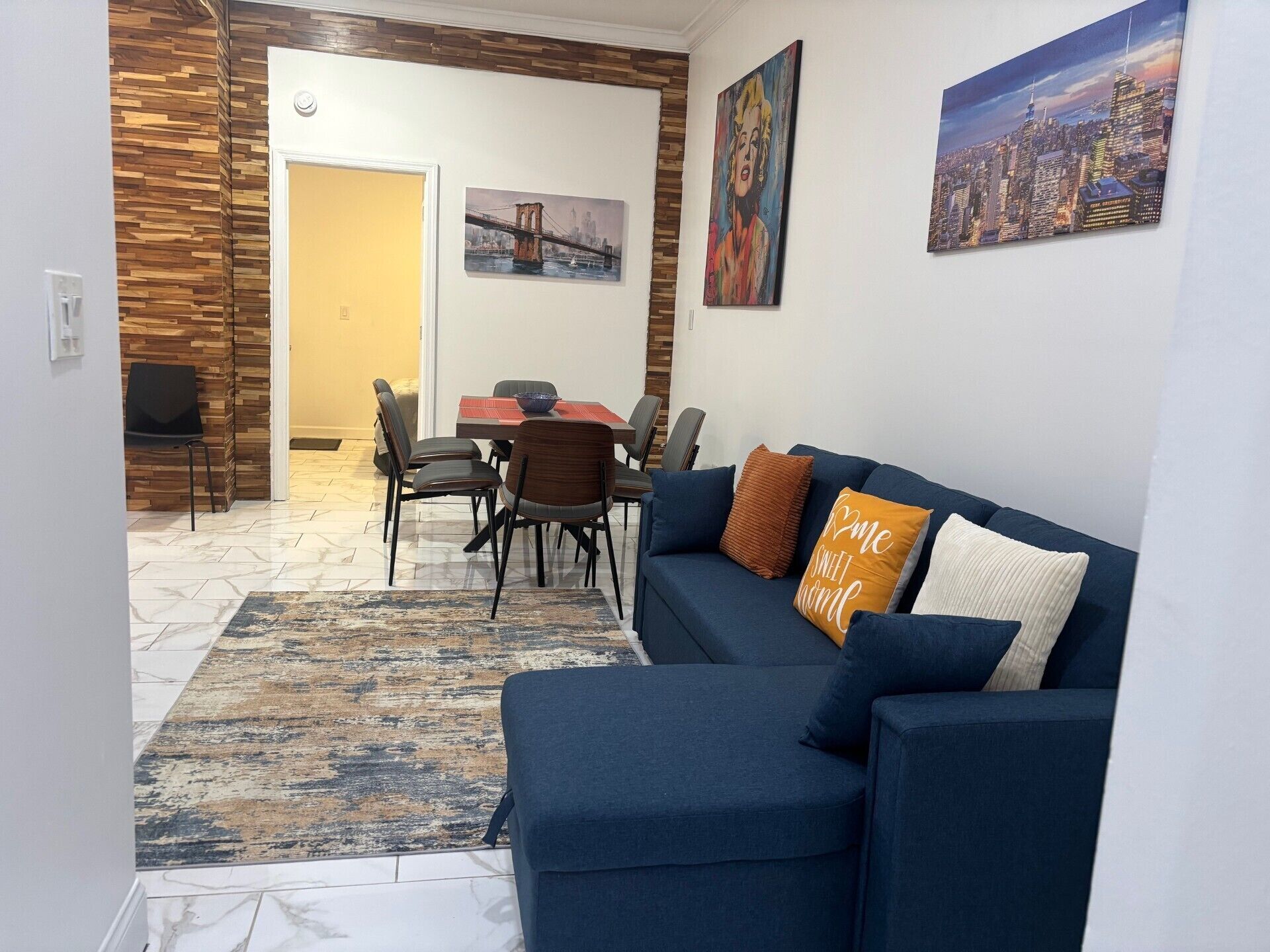 A living room with a blue sofa, a dining table with chairs, and a cityscape painting on the wall.