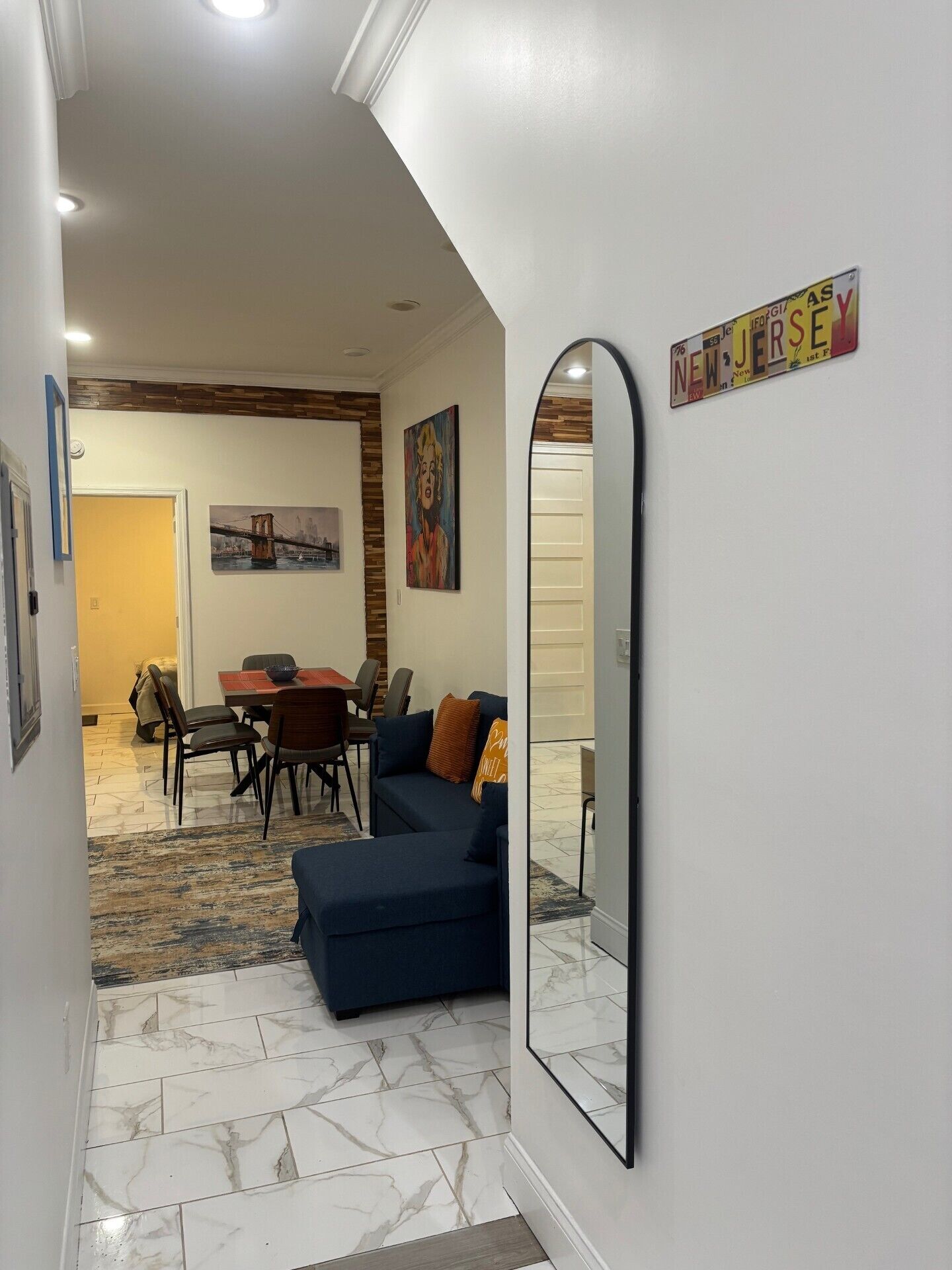 A living room with a sofa, a dining table, and chairs. There is a mirror on the wall and a painting above the sofa.