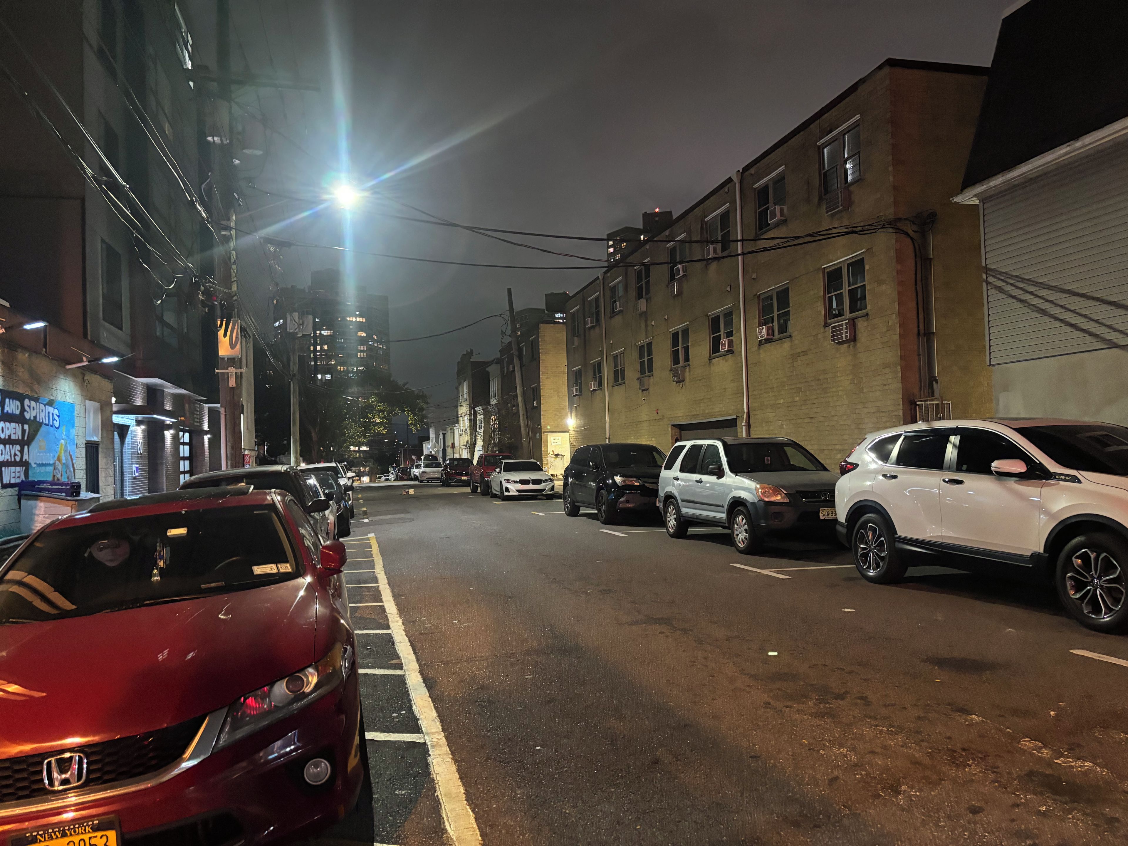A nighttime street scene with parked cars and buildings.