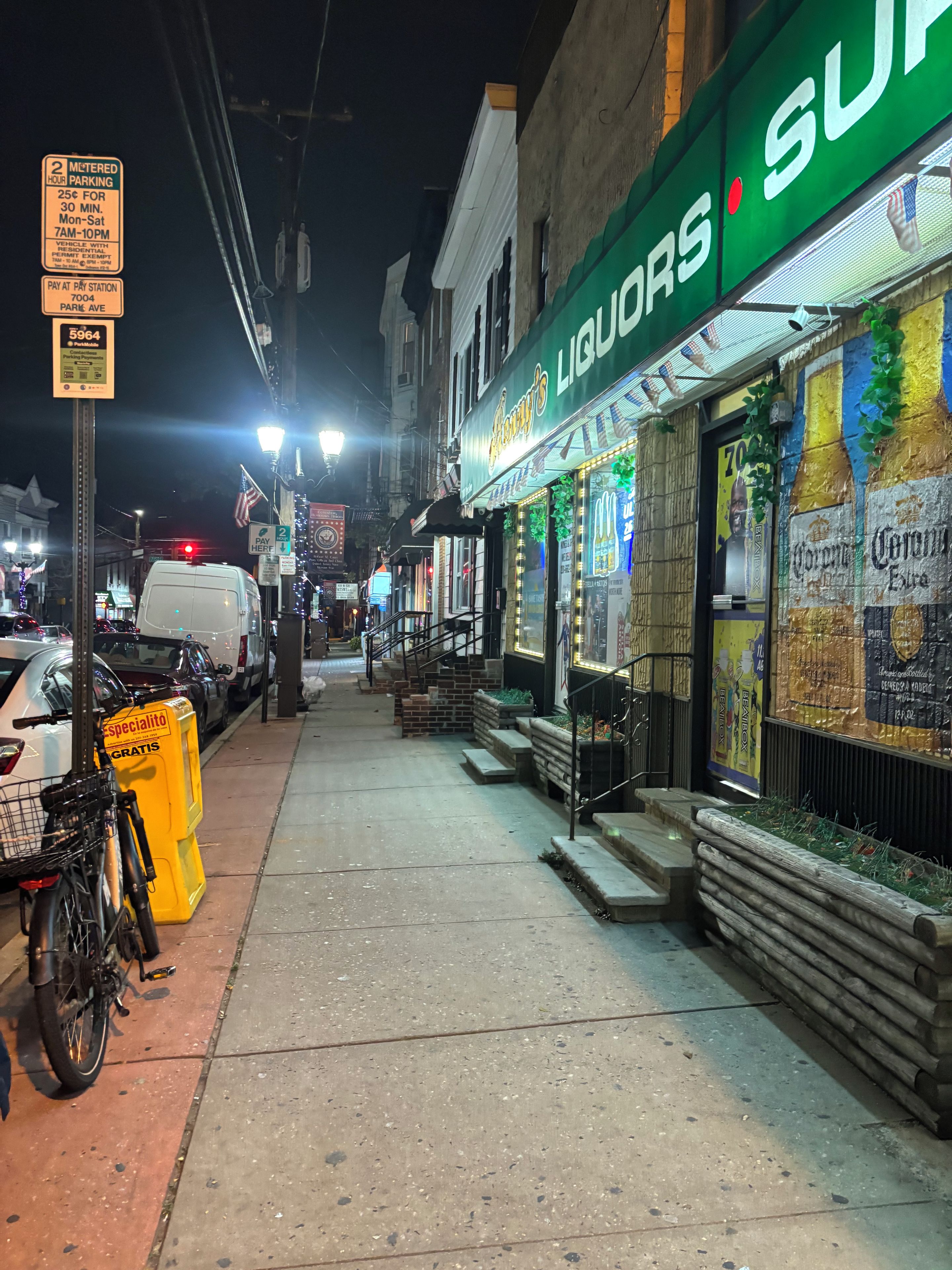A nighttime street scene with a liquor store named 'Liqueurs' and a parked white van.