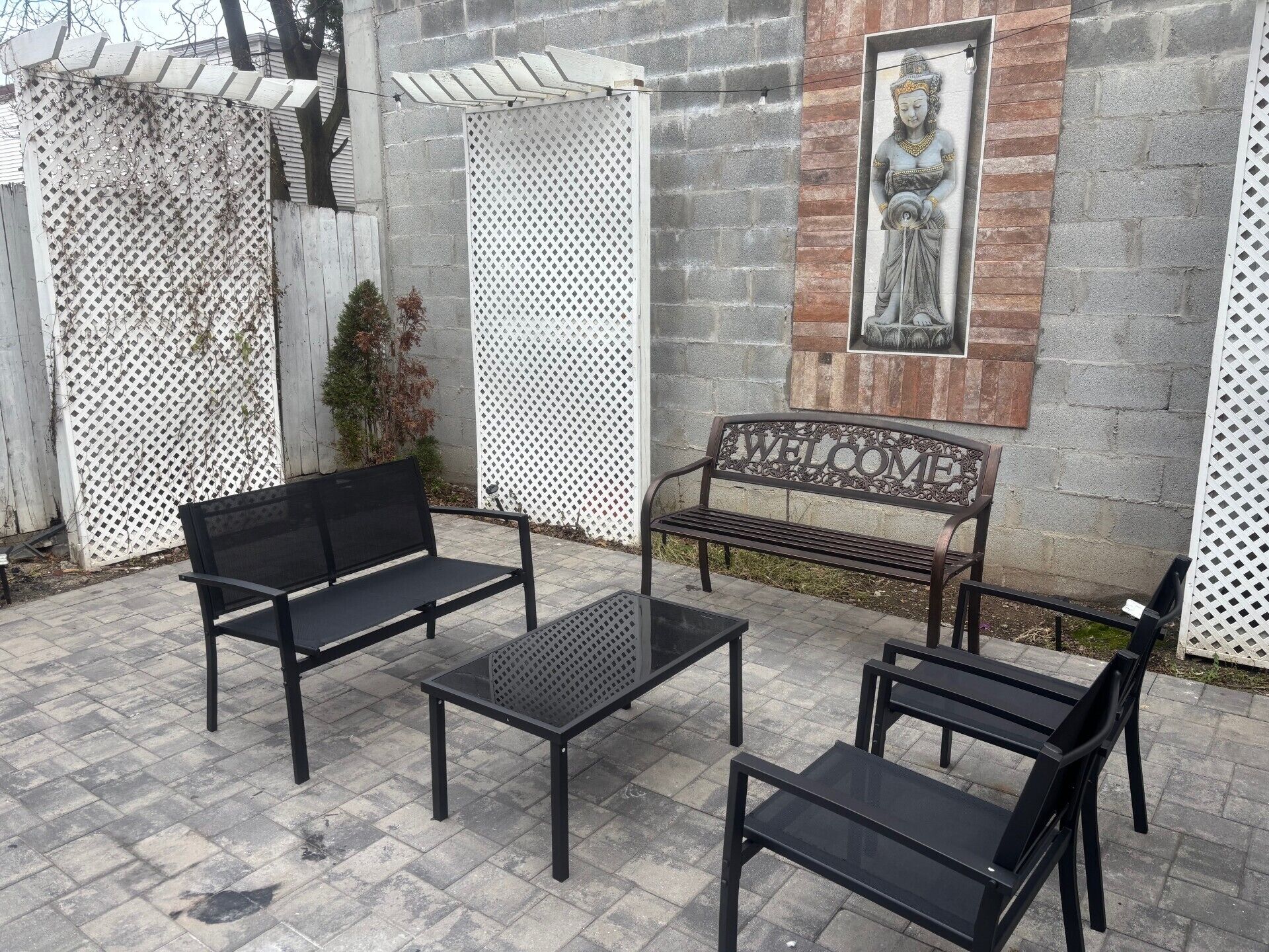 An outdoor seating area with two black metal benches and a matching table, surrounded by a white lattice fence.