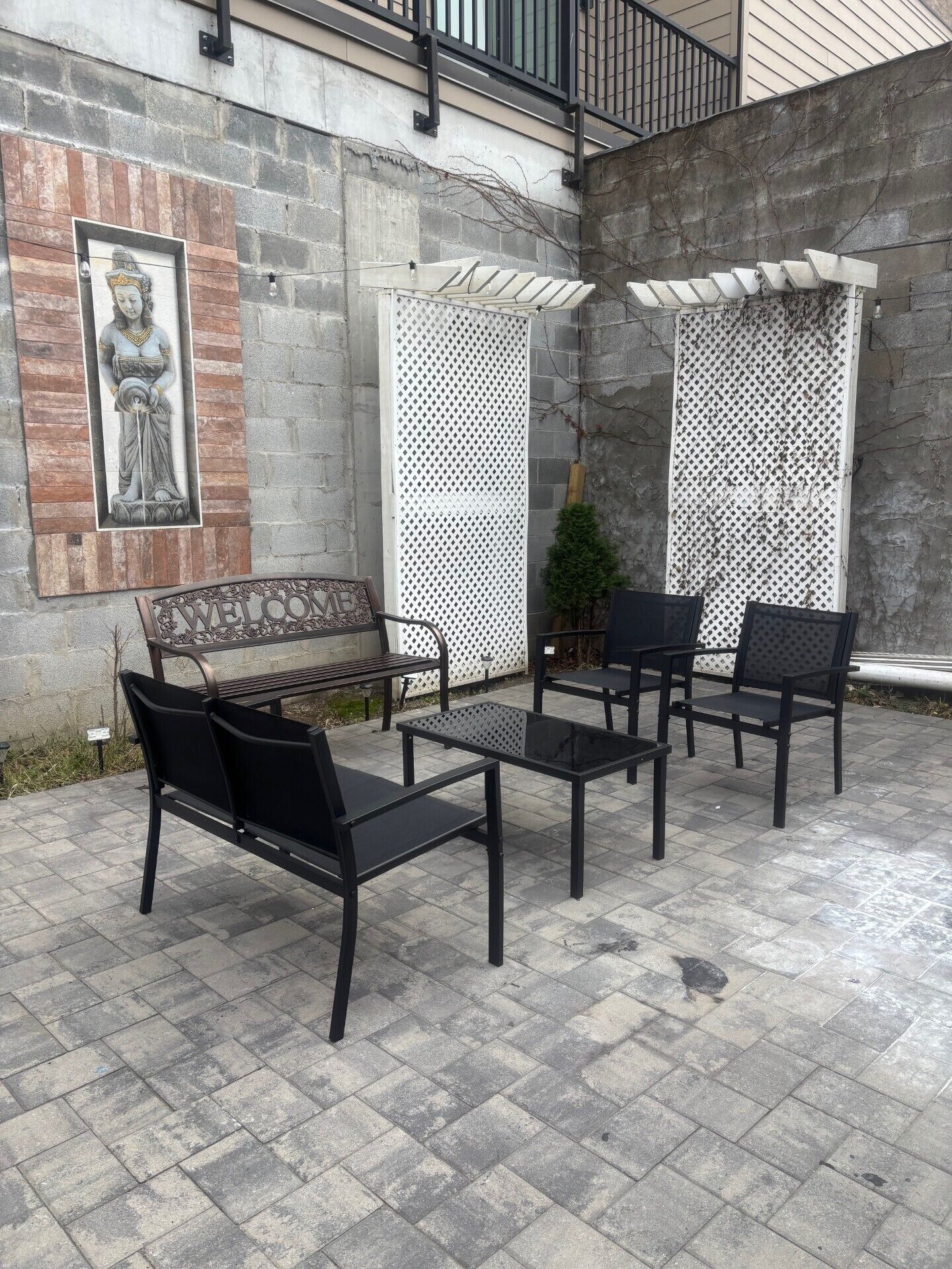 Zona exterior amb seients, una cadira i algunes cadires, una paret decorativa amb una estàtua, i una estructura de celosies.