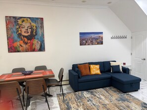 Een moderne woonkamer met een eethoek, een stadslandschap schilderij en een loft-stijl plafond.