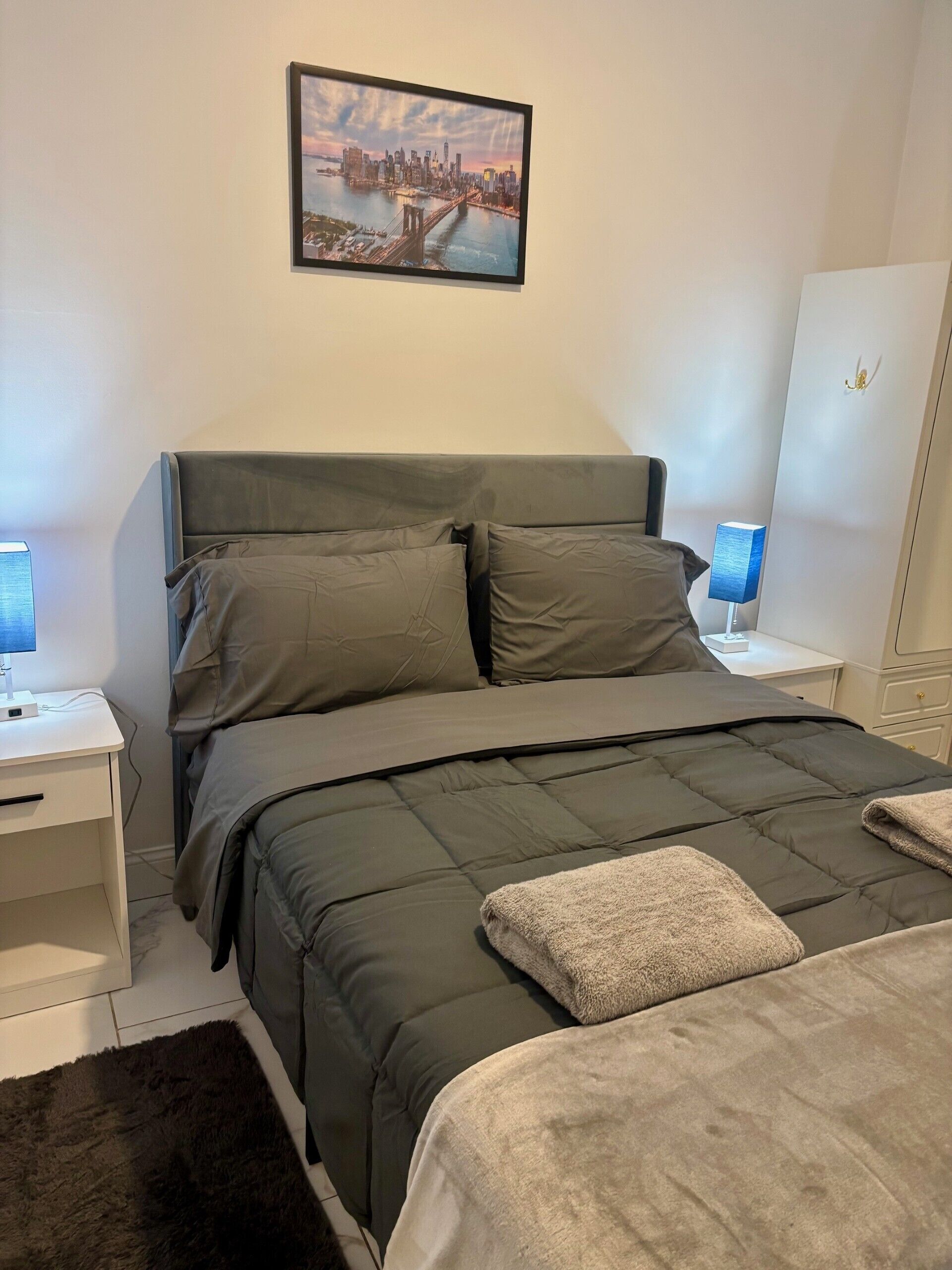 Een slaapkamer met een bed, nachtkastje, lamp, kledingkast en een ingelijst schilderij aan de muur.