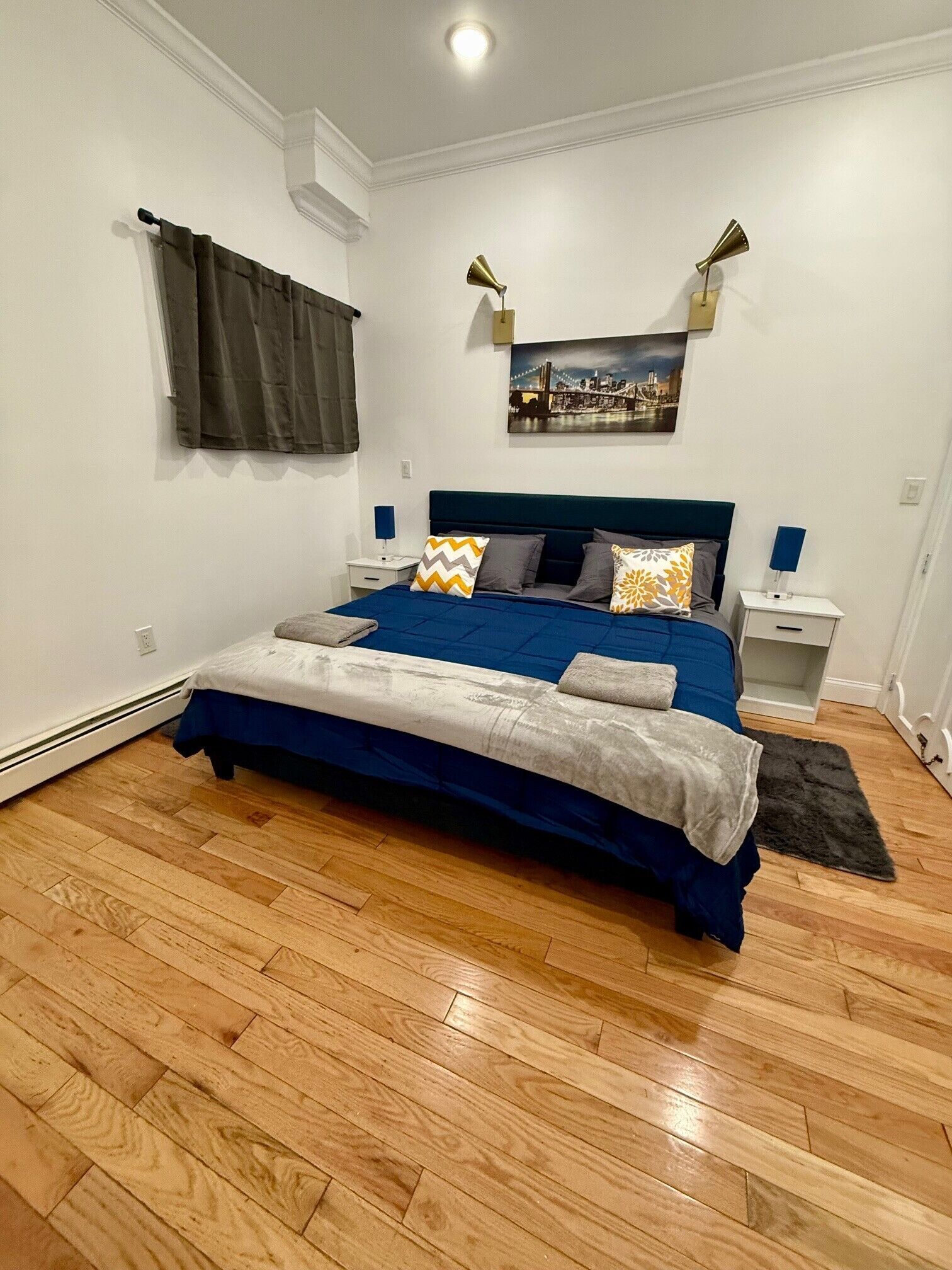 A bedroom with a bed, nightstands, a lamp, a painting, and a window with curtains.
