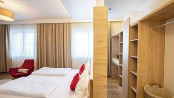 Una habitación de hotel con una cama, una silla roja, un armario de madera y una cesta con la etiqueta 'Juguetes'.