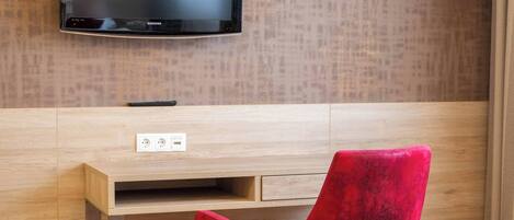 Une chambre moderne avec un bureau en bois, une chaise rouge, un téléviseur fixé au mur et un plancher en bois.