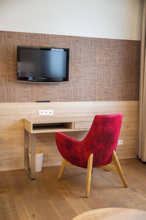 Quarto moderno com escrivaninha de madeira, uma cadeira vermelha, televisão fixada na parede e piso de madeira.