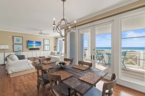 A dining area with a wooden table and chairs, a chandelier, and a view of the beach through large sliding doors. - WaterSound, Resort Pools, Gulf Front, Amazing Views (Watersound)