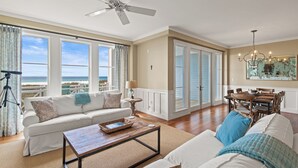 Uma sala de estar espaçosa com um sofá branco, uma mesa de centro e um espaço de jantar com mesa e cadeiras de madeira.