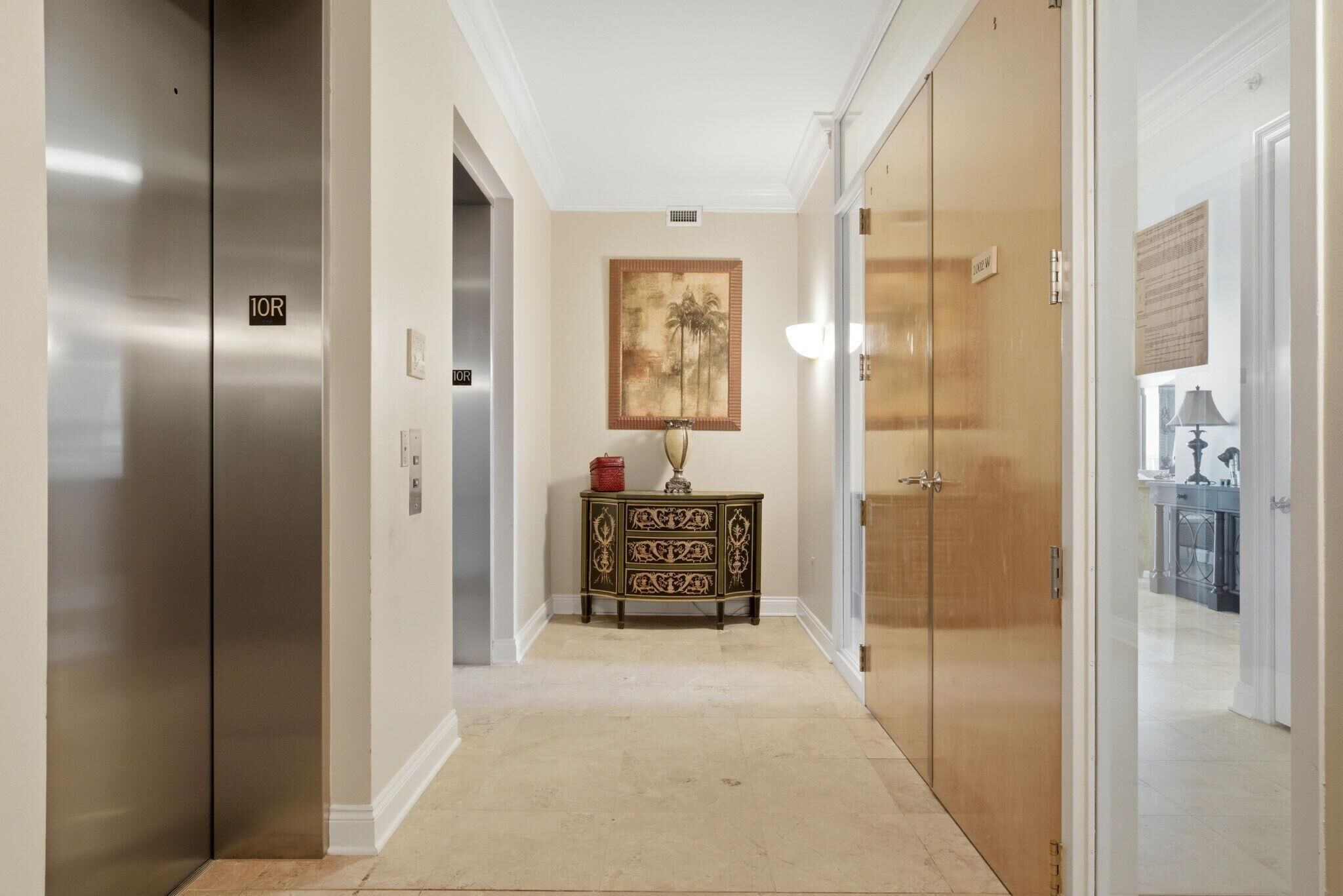 A hallway with an elevator, a decorative cabinet, and a painting on the wall.