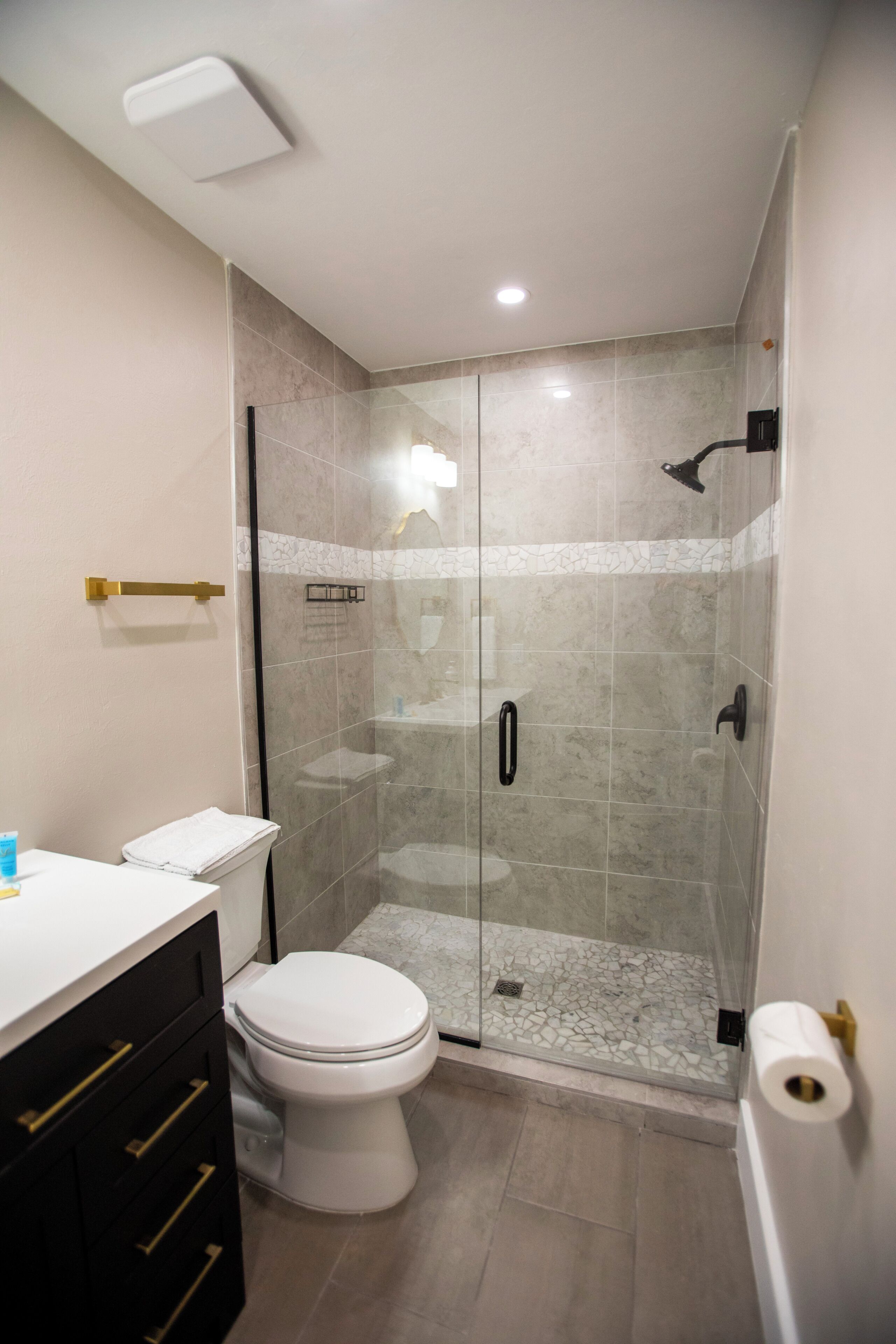 A modern bathroom with a glass-enclosed shower, a toilet, and a vanity with drawers.