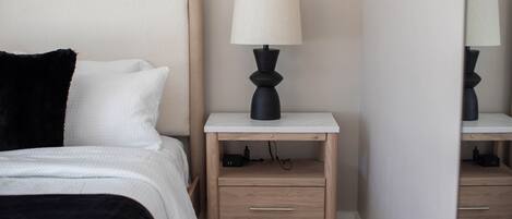 A bedroom with a bed, bedside table, lamp, and a mirror.