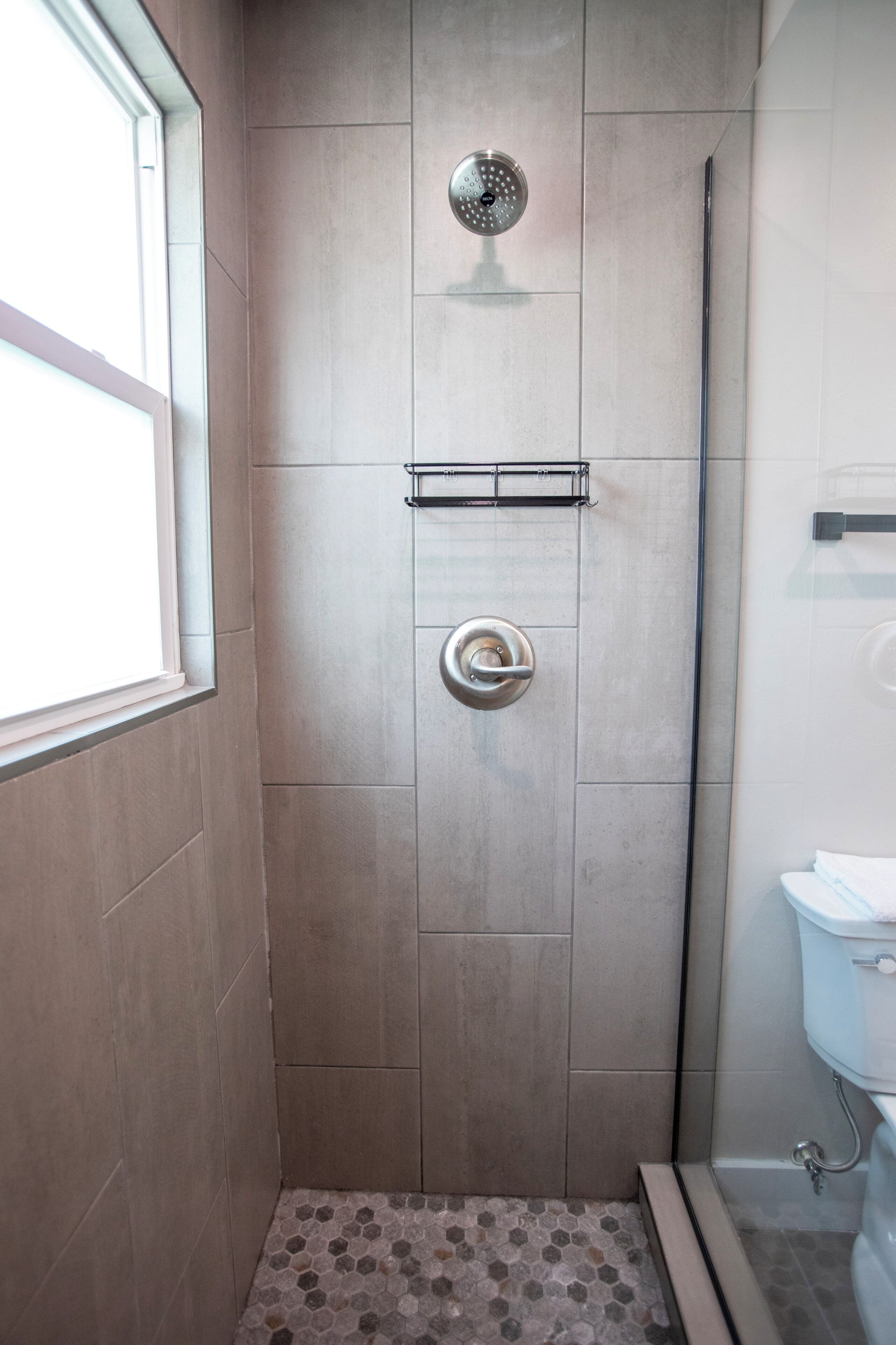 A shower with a glass door, a metal shower head, and a tiled floor.