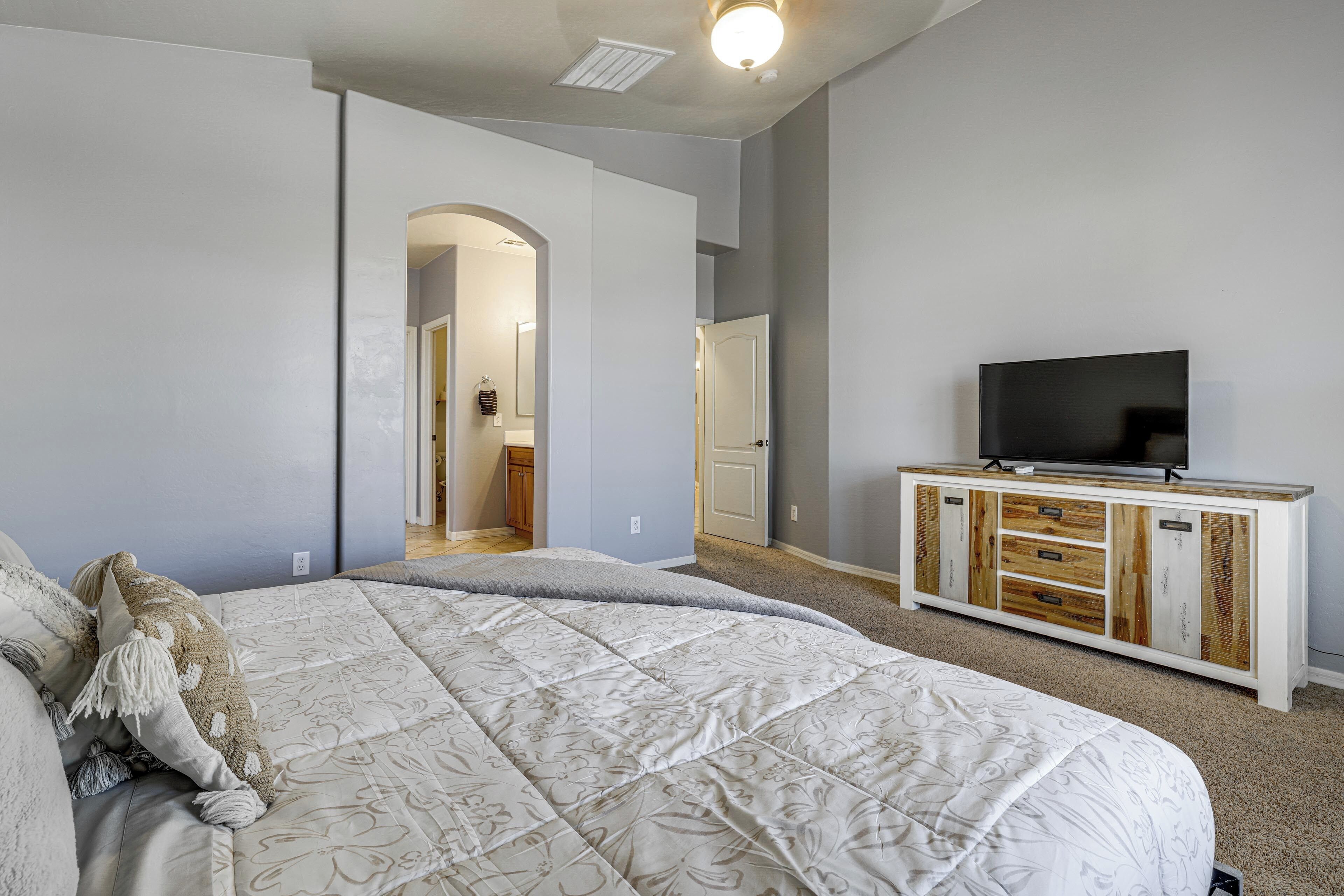 Ein Schlafzimmer mit einem großen Bett, einem Fernseher auf einer Holzkommode und einem Flur, der in ein weiteres Zimmer führt.
