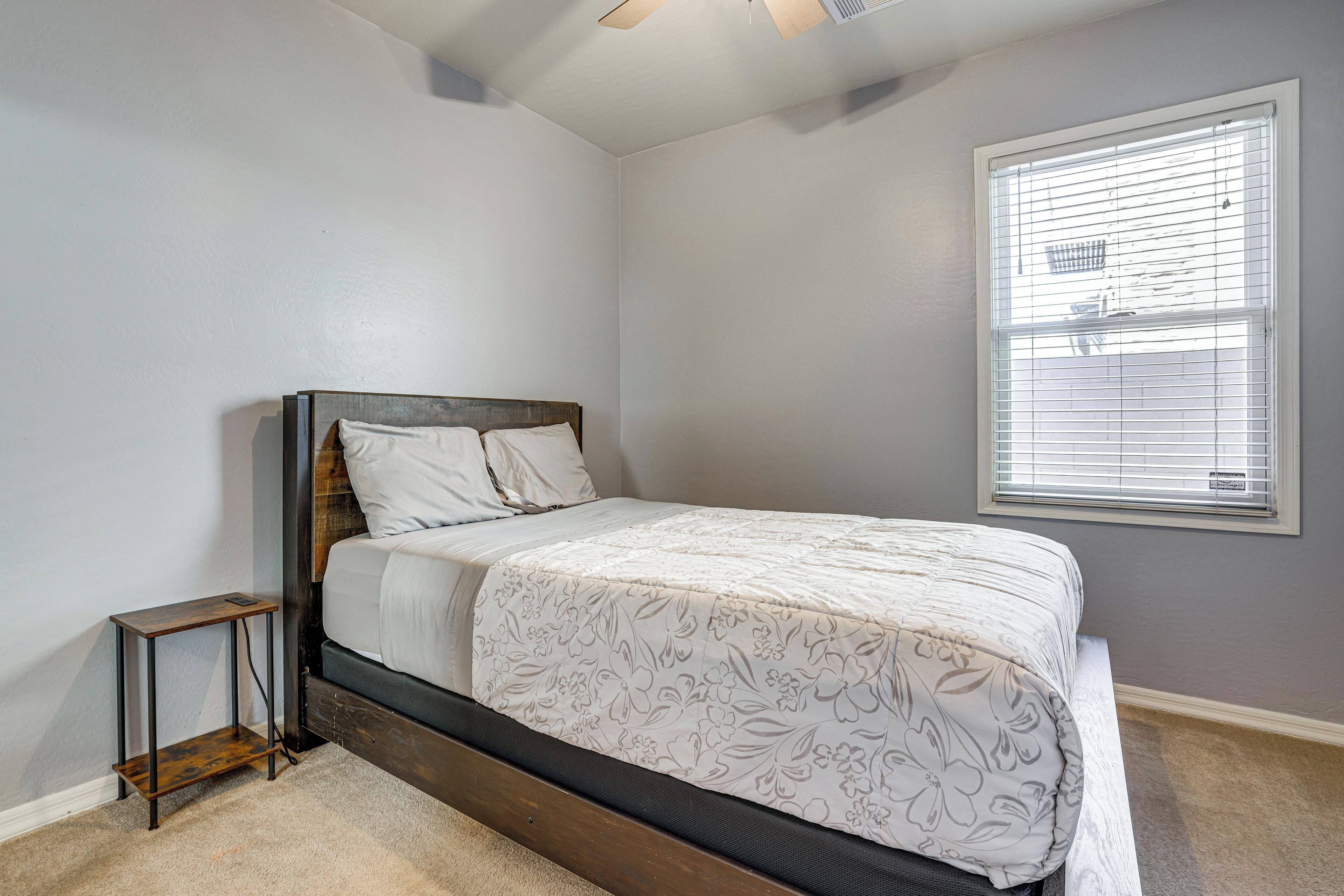 A bedroom with a bed, a small side table, a window with blinds, and a ceiling fan.