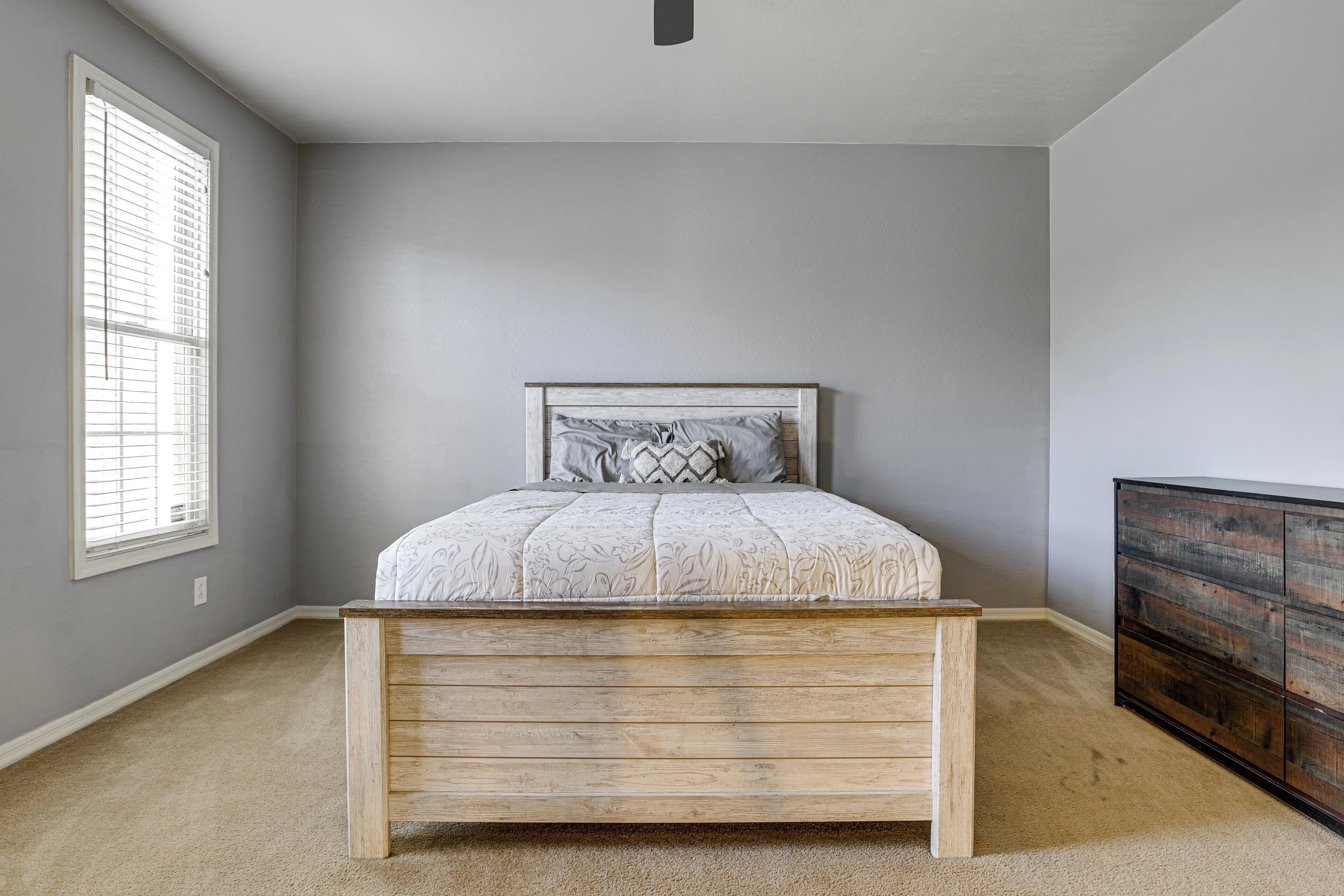 A bedroom with a bed, a dresser, a window with blinds, and a carpeted floor.