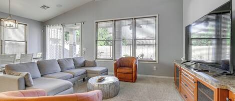 Una sala de estar con un sofá modular, un otoman redondo, un sillón de cuero, un televisor y una cocina con mostrador.